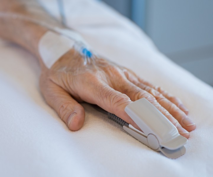 Hand of senior patient with oxygen saturation probe and intravenous line. Close up of mature hand hospitalized and undergoing treatment at hospital. Senior patient lying on bed in hospital.
